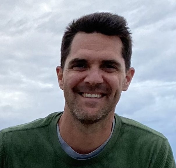 Smiling person wearing a green shirt against a cloudy sky